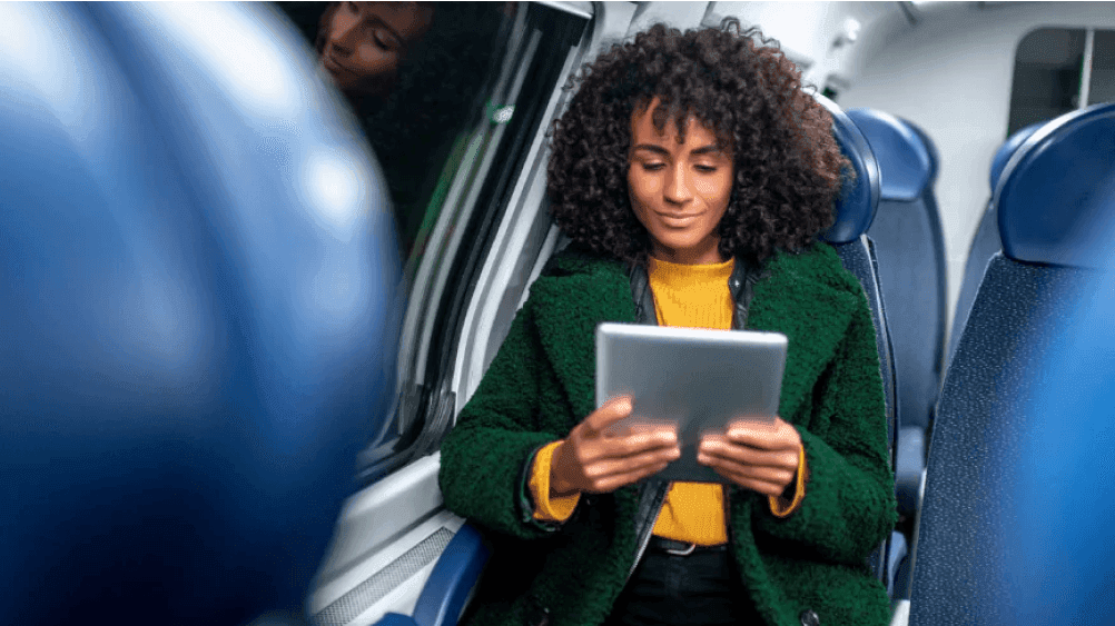 Eine Frau sitzt im Zug und schaut auf ein Tablet.