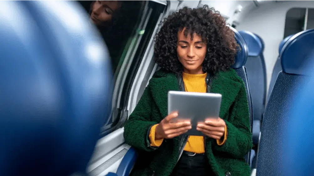 Eine Frau sitzt im Zug und schaut auf ein Tablet.